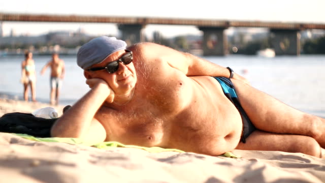 big-bellied-man-is-resting-on-the-beach-stock-video.jpg